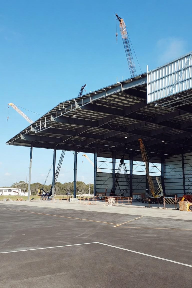Aircraft hangar under construction with steel frame and cranes erecting the roof structure