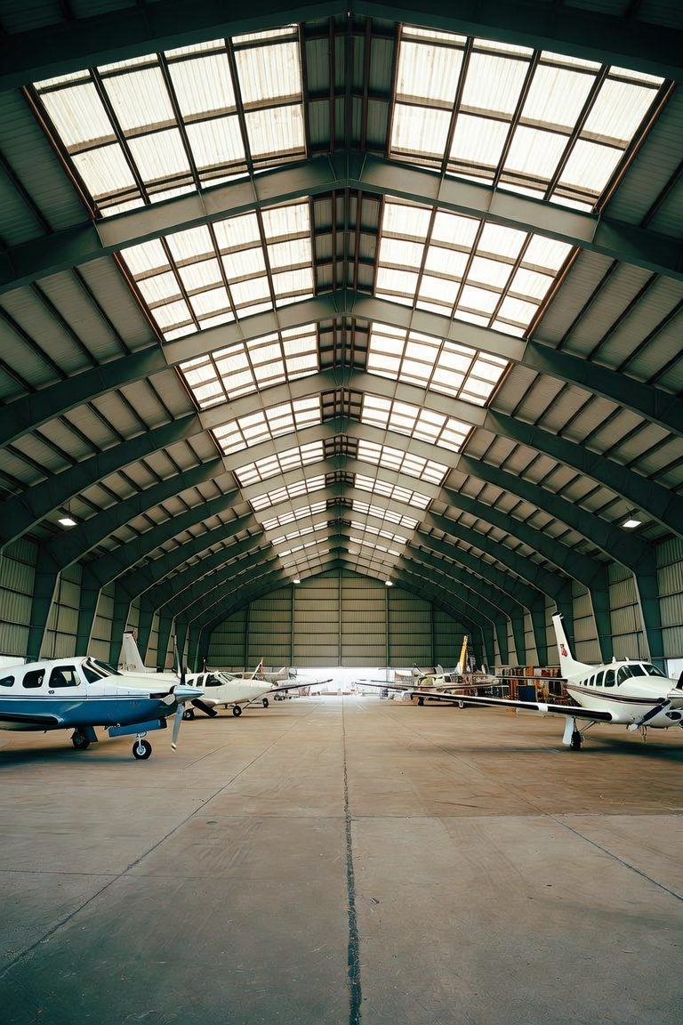 Row of general aviation aircraft parked inside a large arched aircraft hangar with a skylight roof