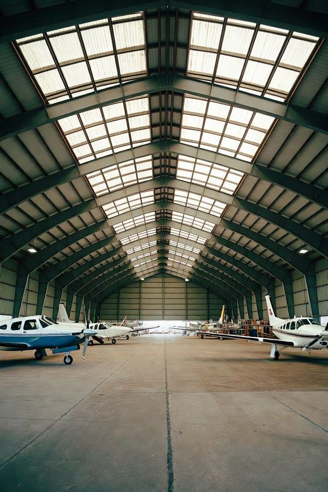 General aviation hangar interior with piston aircraft parked under an arched steel roof